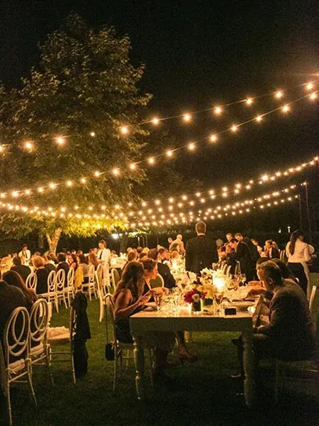 Warm string lighting installed across an outdoor event tent after sunset